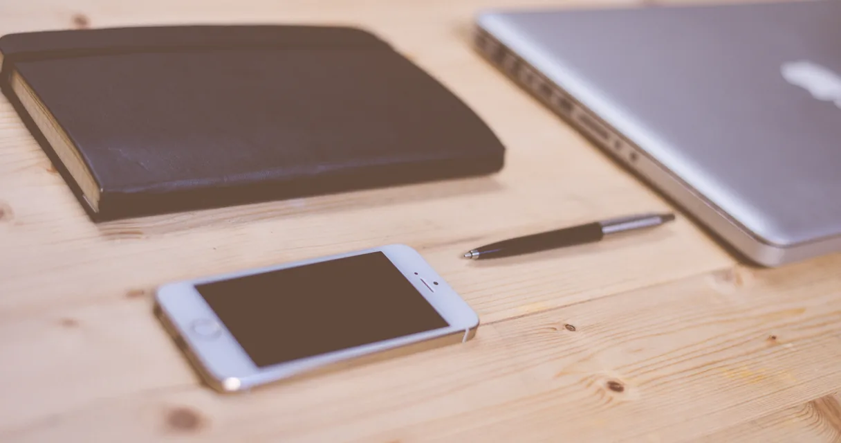 Smartphone, notebook e caderno sobre uma mesa de madeira, ilustrando como limpar o celular de vírus